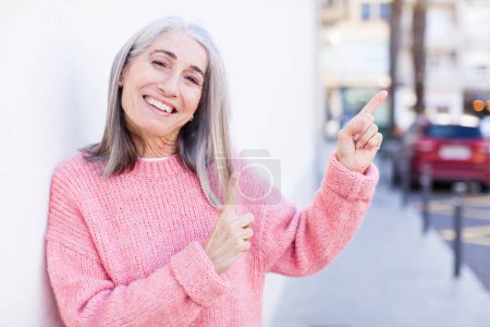 Foto de Jubilado bastante mujer pelo blanco sintiéndose alegre y sorprendido, sonriendo con una expresión conmocionada y señalando a un lado - Imagen libre de derechos