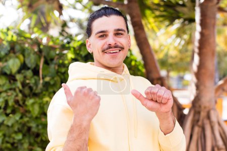 Photo for Young cool man smiling cheerfully and casually pointing to copy space on the side, feeling happy and satisfied - Royalty Free Image
