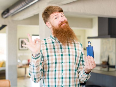 Photo for Red hair man feeling happy, showing approval with okay gesture with a vaper - Royalty Free Image