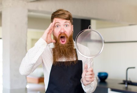 Téléchargez les photos : Homme aux cheveux roux regardant heureux, étonné et surpris dans une cuisine. concept de chef - en image libre de droit