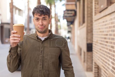 Photo for Young handsome man feeling sad and whiney with an unhappy look and crying. take away coffee concept - Royalty Free Image