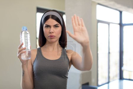 Téléchargez les photos : Jolie jeune femme regardant sérieusement montrant la paume ouverte faisant geste d'arrêt. concept de bouteille d'eau - en image libre de droit