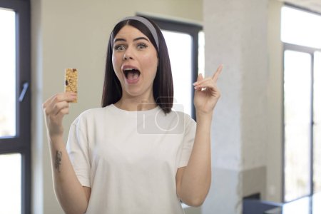 Photo for Pretty young woman feeling like a happy and excited genius after realizing an idea. fitness cereal bar concept - Royalty Free Image