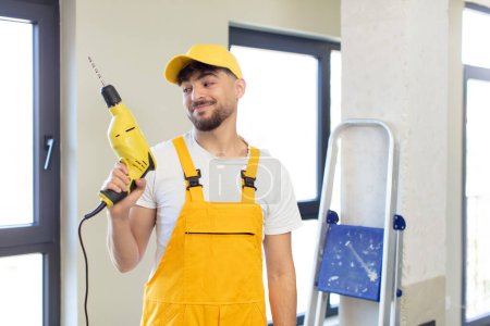 Photo for Young handsome man smiling and looking with a happy confident expression. handyman and drill concept - Royalty Free Image