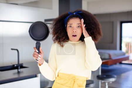 Photo for Pretty afro black woman feeling extremely shocked and surprised. home chef concept - Royalty Free Image