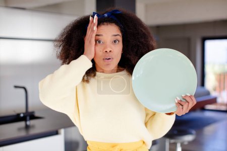Photo for Pretty afro black woman feeling extremely shocked and surprised. home chef concept - Royalty Free Image