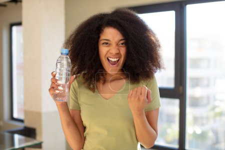 Téléchargez les photos : Jolie afro femme noire à l'air en colère, agacé et frustré. concept de bouteille d'eau - en image libre de droit