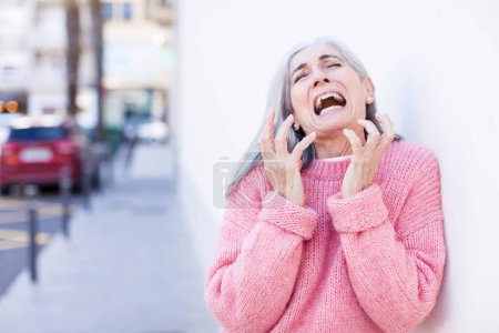 Foto de Senior jubilado bastante blanco cabello mujer buscando desesperado y frustrado, estresado, infeliz y molesto, gritando y gritando - Imagen libre de derechos