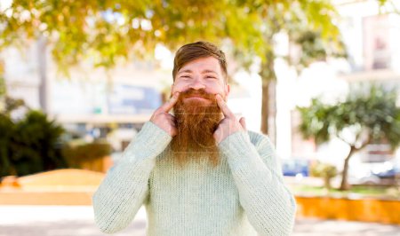 Photo for Red hair bearded man smiling confidently pointing to own fake smile - Royalty Free Image