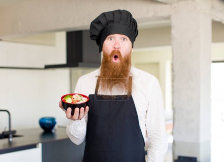 Photo for Red hair man feeling extremely shocked and surprised with a ramen bowl. chef concept - Royalty Free Image