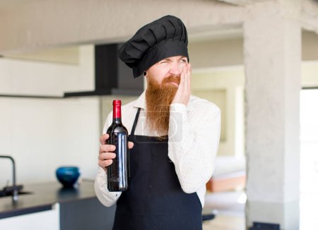 Foto de Hombre de pelo rojo sentirse aburrido, frustrado y soñoliento después de un cansancio con una botella de vino. concepto de chef - Imagen libre de derechos