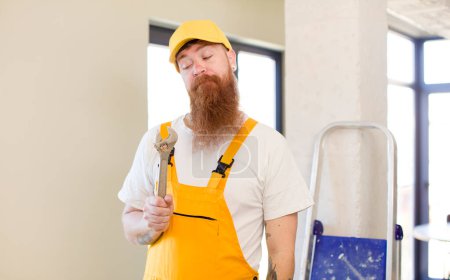 Téléchargez les photos : Homme aux cheveux roux souriant et regardant avec une expression heureuse et confiante réparer la maison. concept bricoleur - en image libre de droit