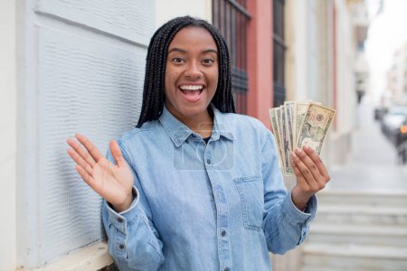 Téléchargez les photos : Afro noir femme se sentant heureux et étonné de quelque chose d'incroyable. concept des billets en dollars - en image libre de droit