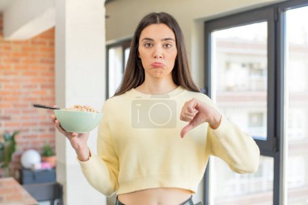 Photo for Pretty young model feeling cross,showing thumbs down. breakfast bowl concept - Royalty Free Image