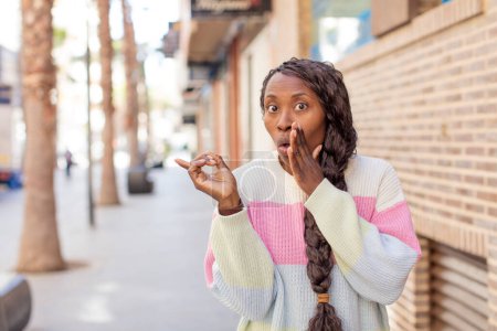 Téléchargez les photos : Afro jolie femme noire se sentant surprise avec une expression choquée et pointant vers le côté - en image libre de droit