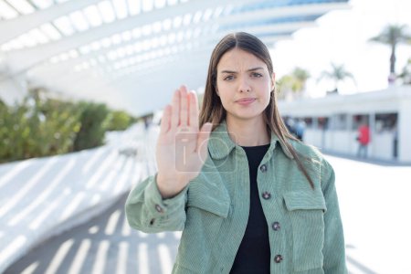 Photo for Young pretty woman looking serious, stern, displeased and angry showing open palm making stop gesture - Royalty Free Image