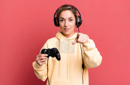 Foto de Mujer rubia bonita apuntando a la cámara elegirte. gamer con auriculares y un controlador - Imagen libre de derechos