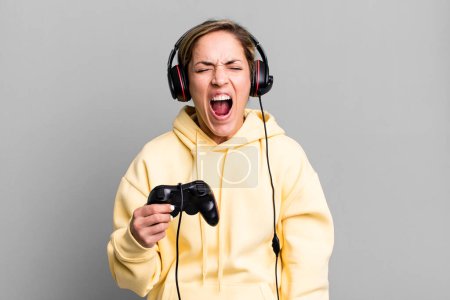 Photo for Pretty blonde woman shouting aggressively, looking very angry. gamer with headset and a controller - Royalty Free Image