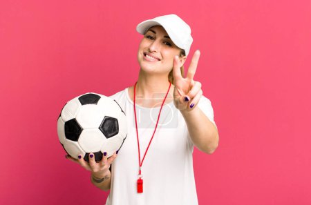 Téléchargez les photos : Jeune jolie femme souriante et heureuse, geste de victoire ou de paix. concept entraîneur de football - en image libre de droit
