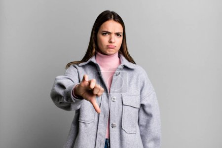 Photo for Pretty young adult woman feeling cross, angry, annoyed, disappointed or displeased, showing thumbs down with a serious look - Royalty Free Image