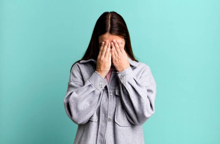 Photo for Pretty young adult woman feeling sad, frustrated, nervous and depressed, covering face with both hands, crying - Royalty Free Image