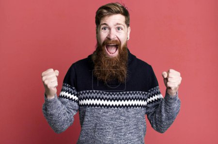 Foto de Barba larga y cabello rojo hombre sintiéndose sorprendido, riendo y celebrando el éxito - Imagen libre de derechos