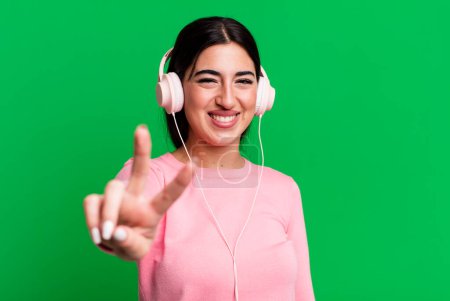 Foto de Sonriendo y luciendo feliz, haciendo gestos de victoria o paz. escuchar música con auriculares - Imagen libre de derechos
