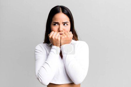 Photo for Hispanic pretty woman looking worried, anxious, stressed and afraid, biting fingernails and looking to lateral copy space - Royalty Free Image