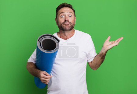 Photo for Middle age man feeling puzzled and confused and doubting. with a yoga matt. fitness concept - Royalty Free Image