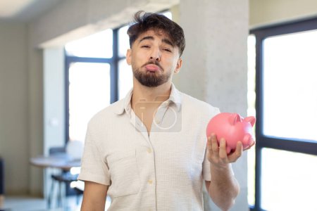 Photo for Young handsome man feeling sad and whiney with an unhappy look and crying. piggy bank concept - Royalty Free Image