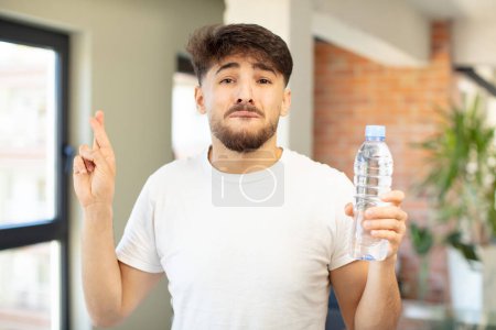 Photo for Young handsome man crossing fingers and hoping for good luck. water bottle concept - Royalty Free Image