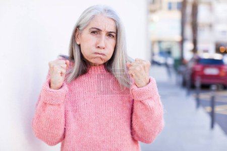 Téléchargez les photos : Senior retraité jolie femme aux cheveux blancs regardant confiant, en colère, fort et agressif, avec les poings prêts à se battre en position de boxe - en image libre de droit