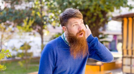 Photo for Red hair bearded man looking serious and curious, listening, trying to hear a secret conversation or gossip, eavesdropping - Royalty Free Image