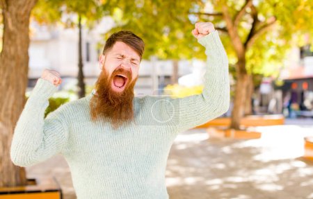 Photo for Red hair bearded man feeling happy, positive and successful, celebrating victory, achievements or good luck - Royalty Free Image