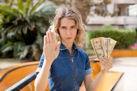 Foto de Pretty woman looking serious showing open palm making stop gesture. dollar banknotes concept - Imagen libre de derechos