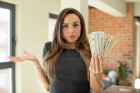 Téléchargez les photos : Pretty woman shrugging, feeling confused and uncertain. dollar banknotes concept - en image libre de droit