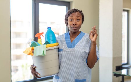 Photo for Black afro woman crossing fingers and hoping for good luck with clean products. housekeeper concept - Royalty Free Image