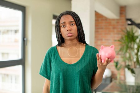 Photo for Black afro woman feeling sad and whiney with an unhappy look and crying. piggy bank concept - Royalty Free Image