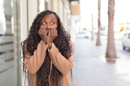 Photo for Afro pretty black woman looking worried, anxious, stressed and afraid, biting fingernails and looking to lateral copy space - Royalty Free Image
