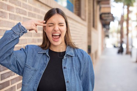 Téléchargez les photos : Jeune jolie femme regardant malheureux et stressé, geste suicidaire faisant signe d'arme à feu avec la main, pointant vers la tête - en image libre de droit