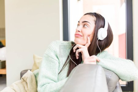 Téléchargez les photos : Jolie jeune femme qui écoute de la musique avec un casque. design intérieur de la maison - en image libre de droit