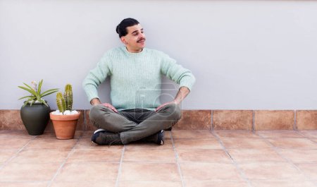 Téléchargez les photos : Jeune bel homme gardant et assis sur le sol à l'extérieur - en image libre de droit
