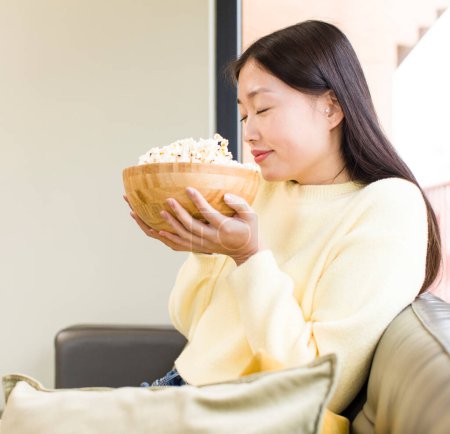 Foto de Asiático bonita mujer comer palomitas de maíz y viendo un película en casa - Imagen libre de derechos