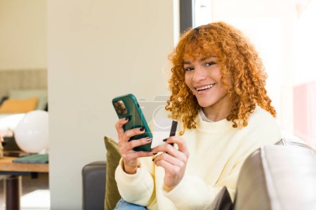 Téléchargez les photos : Jeune rousse cheveux latins jolie femme en utilisant un smartphone à la maison - en image libre de droit