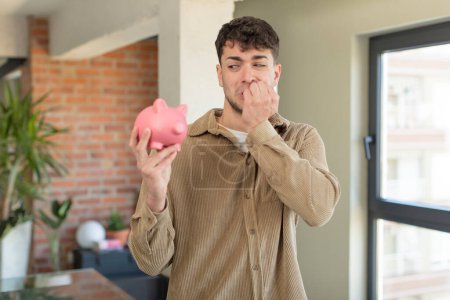 Photo for Young handsome man feeling scared, worried or angry and looking to the side. piggy bank concept - Royalty Free Image