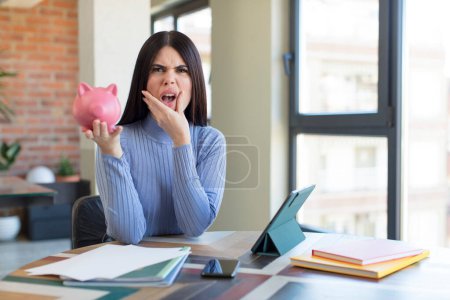 Photo for Pretty young woman with mouth and eyes wide open and hand on chin. piggy bank concept - Royalty Free Image