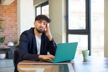 Photo for Young handsome man feeling sad and whiney with an unhappy look and crying. freelance concept with laptop - Royalty Free Image