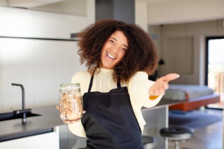 Foto de Mujer negra bastante afro sonriendo felizmente y ofreciendo o mostrando un concepto. concepto de cookies caseras - Imagen libre de derechos