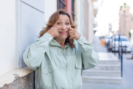 Téléchargez les photos : Femme d'âge moyen souriant et pointant vers son propre faux sourire - en image libre de droit