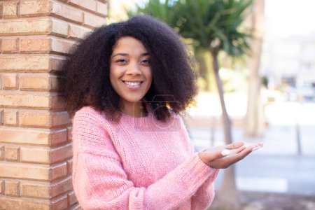 Téléchargez les photos : Afro-américaine jolie femme souriante, confiante, réussie et heureuse, montrant concept ou idée sur l'espace de copie sur le côté - en image libre de droit